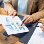 primopiano di una scrivania dove si intravedono due persone, una mostra un grafico ad un'altra