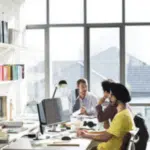 persone in un ufficio grande con grosse vetrate, clienti e impiegati